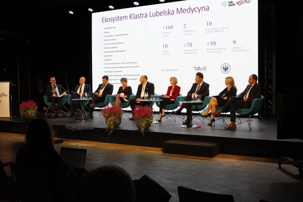 Ósemka panelistów siedzi na fotelach na scenie, pytanie zadaje moderator: Dr Mariusz Sagan