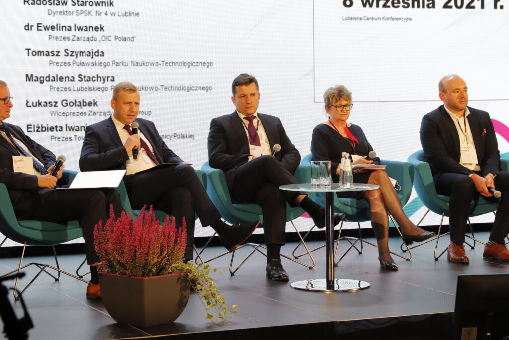 Panelista Damian Malec - z Urzędu Marszałkowskiego Województwa Lubelskiego trzyma mikrofon, wypowiadając się na zadane pytanie przez moderatora dr Mariusza Sagan, obok po prawej stronie siedzi trójka innych panelistów